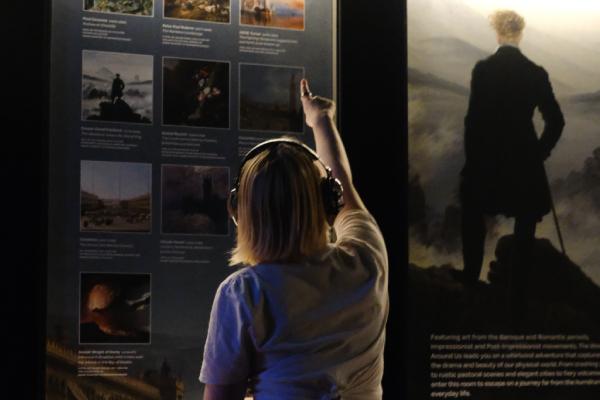 A girl wearing ear defenders is pointing at an informational display in the FRAMELESS immersive gallery.
