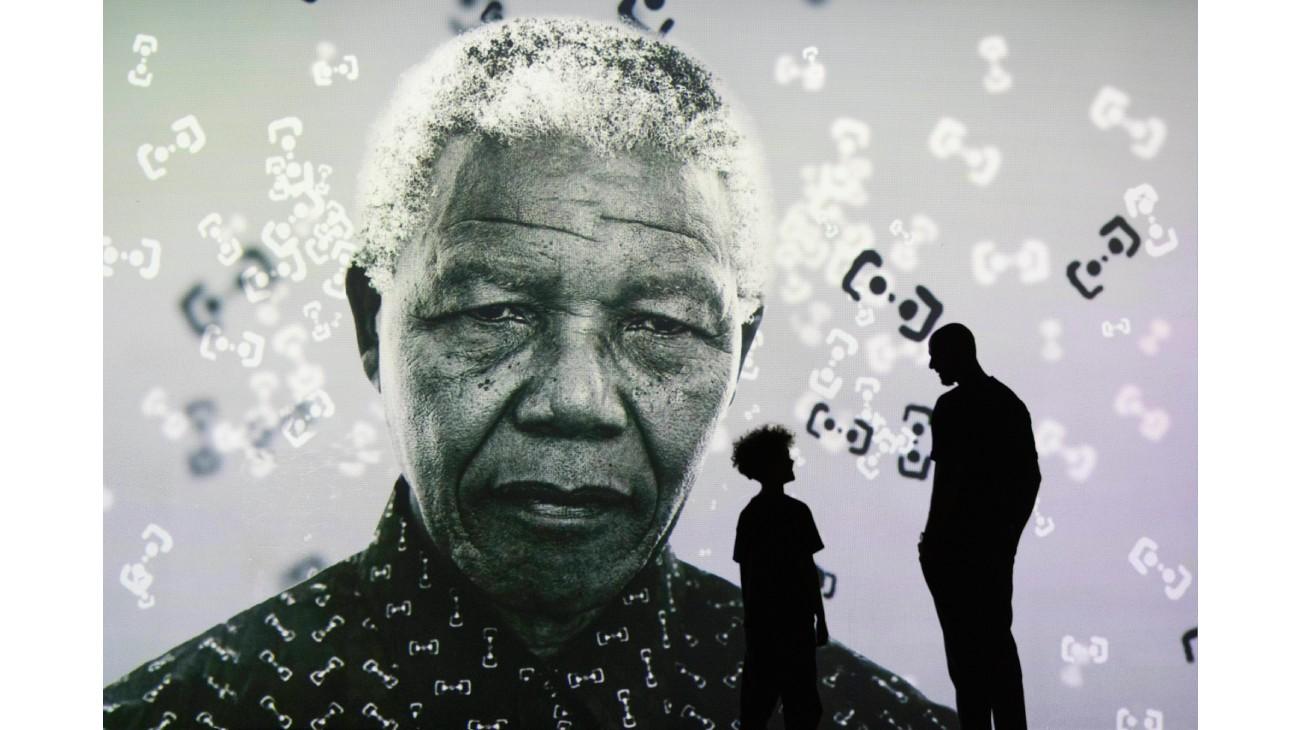 The silhouette of a father and child standing in front of a portrait of Nelson Mandela