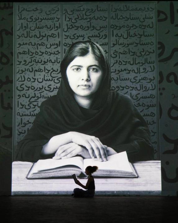 A silhouette of a girl reading a book in front of a portrait of Malala Yousafzai