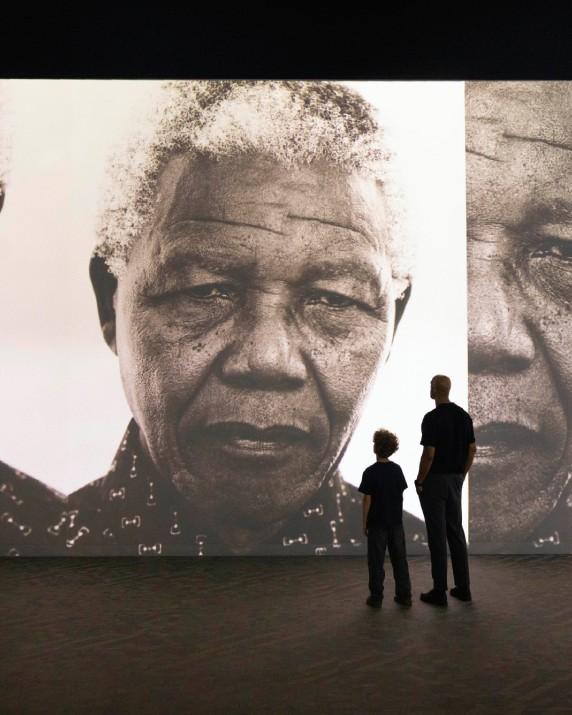 The silhouette of a father and child standing in front of a portrait of Nelson Mandela