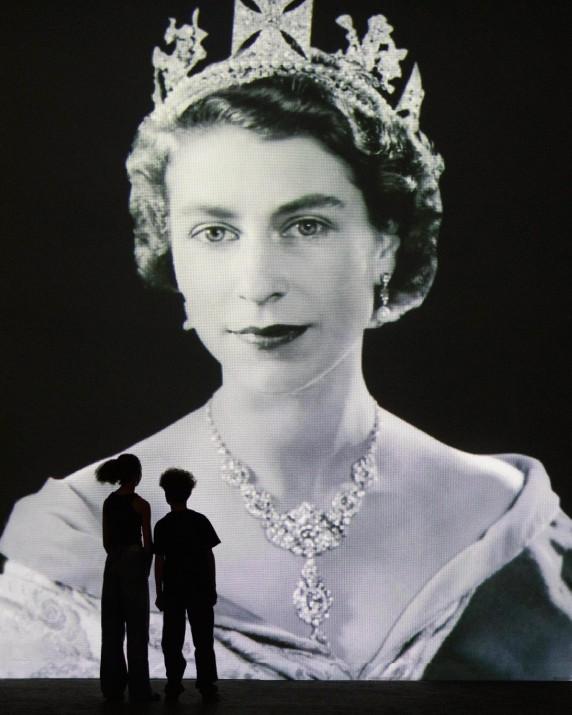 The silhouettes of two children standing in front of a portrait of Queen Elizabeth II